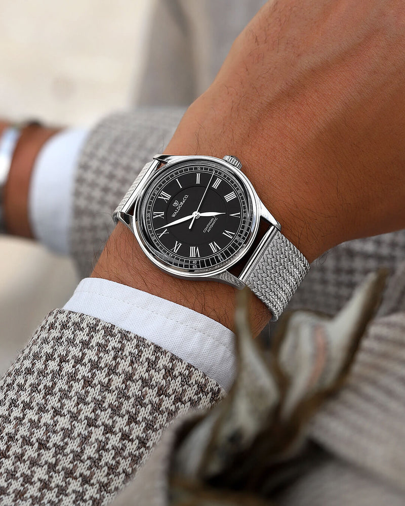 A round Automatic mens watch in Rhodium-plated 316L stainless from Waldor & Co. with black double-layered dial in copper. Curved mineral glass with anti-reflective coating. Miyota 9093 movement. Mesh strap. The model is Continual 39 Amalfi.