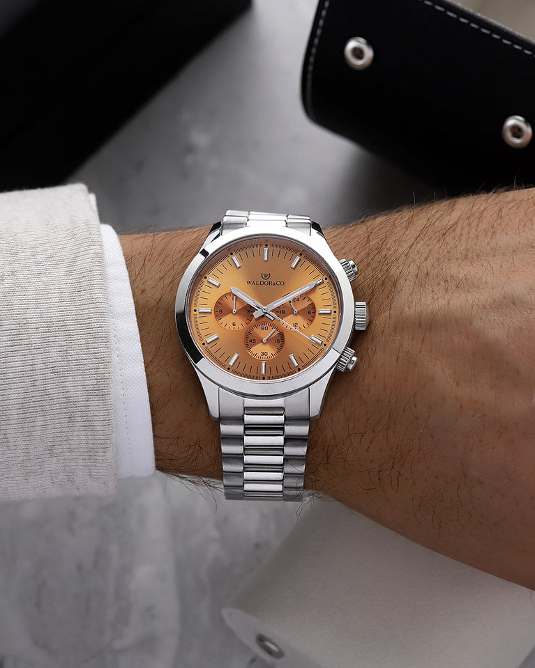 A round mens watch in rhodium-plated silver from Waldor & Co. with orange sunray dial and a second hand. Seiko movement. The model is Chrono 44 Como 44mm.