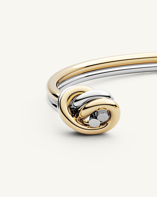 A polished stainless steel bangle in 14k gold from Waldor & Co. One size. The model is Dual Knot Twin Bangle.